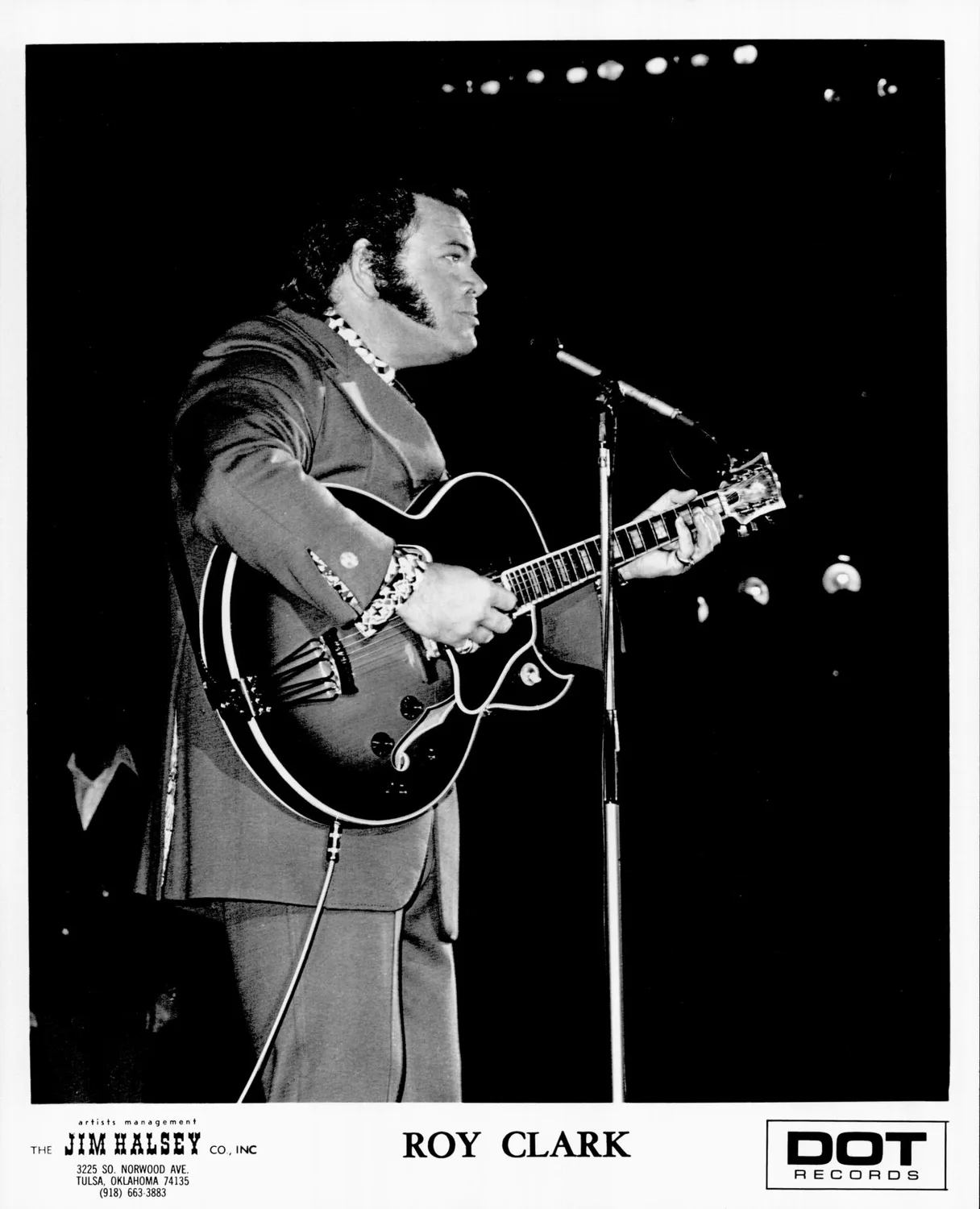 Clark Roy standing, playing guitar in suit.